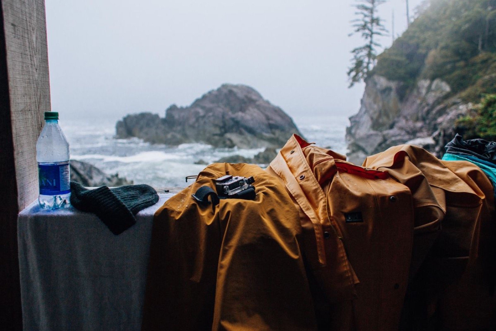 Yellow rain jackets, wool socks and a water bottle drying by a rocky coast