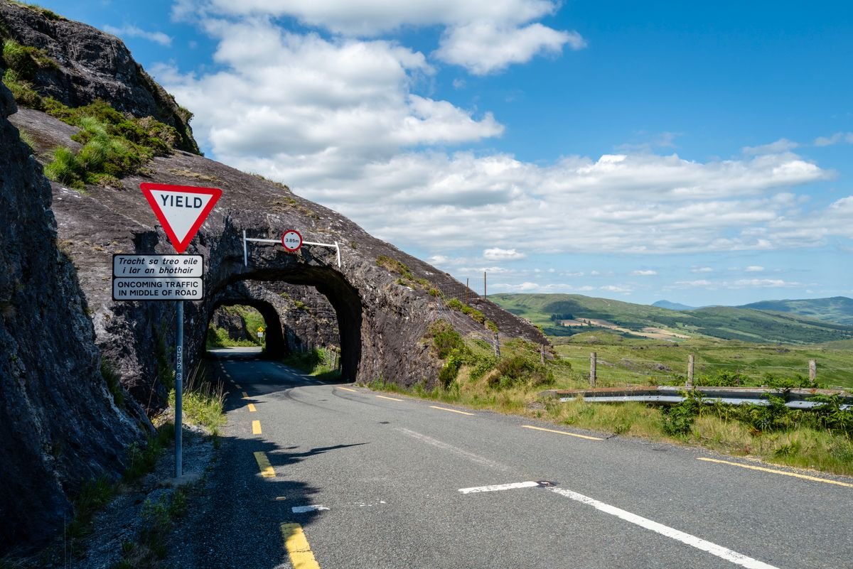 Signposted coast road winding under a rock arch on the Wild Atlantic Way