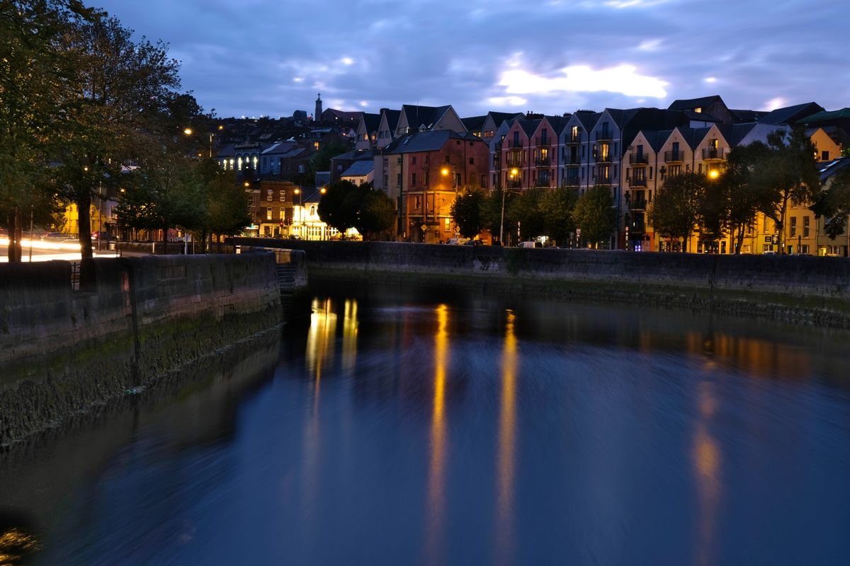 Cork city riverside buildings lit up at dusk with lights reflecting on the River Lee