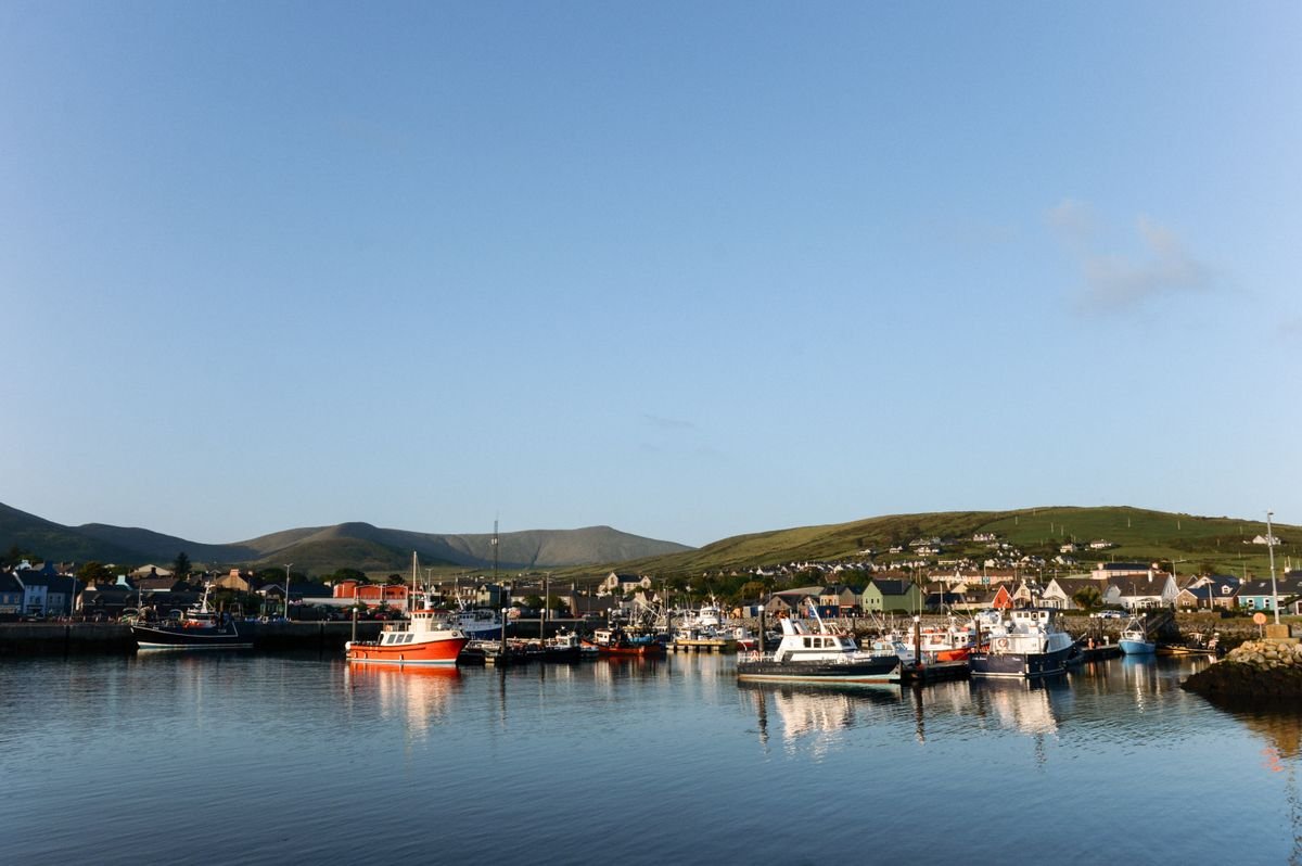 Dingle Harbour at dusk with fishing boats moored and the town and hills behind