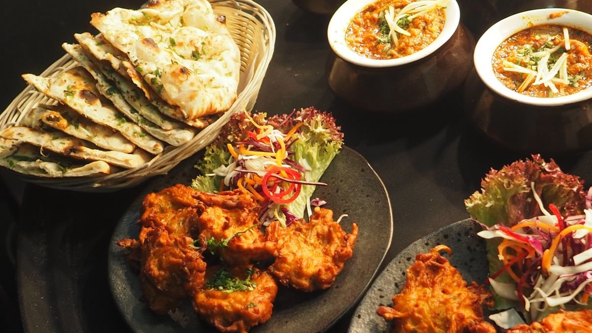 Indian curry dishes with naan, pakoras and side dishes on a table