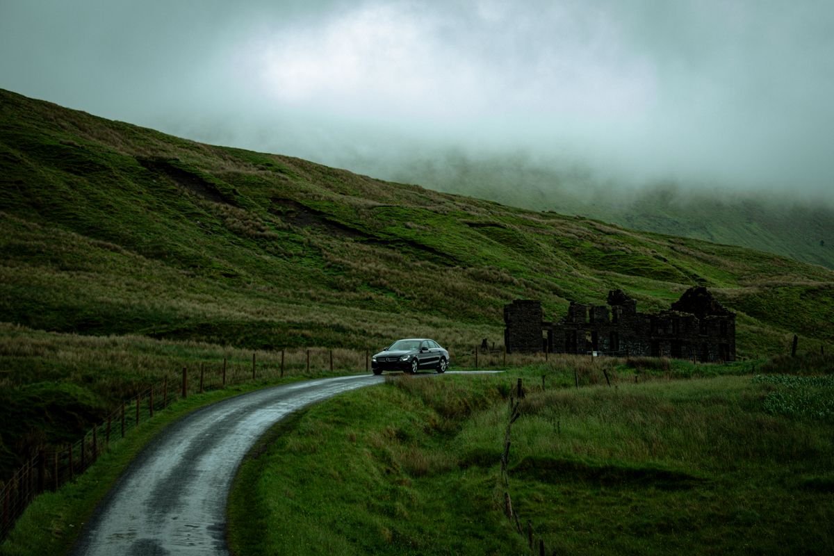 Car on a narrow green rural road in Ireland near stone ruins