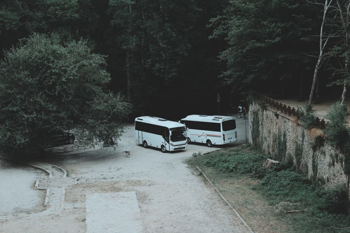 Two tour coaches parked in a car park by a stone wall