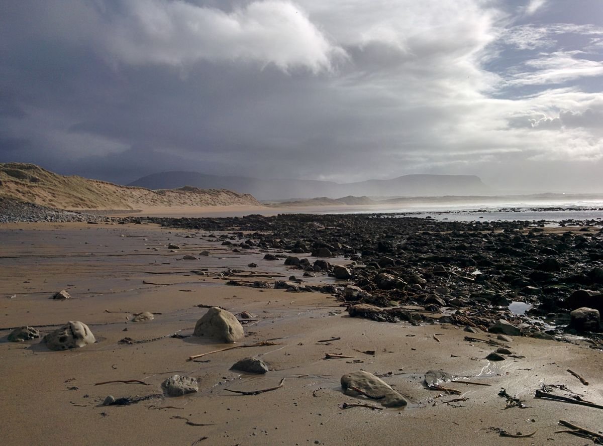 A moody Donegal strand backed by mountains under a bright summer sky