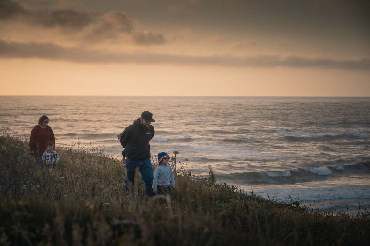 A family with young children walking a grassy coastal path by the sea