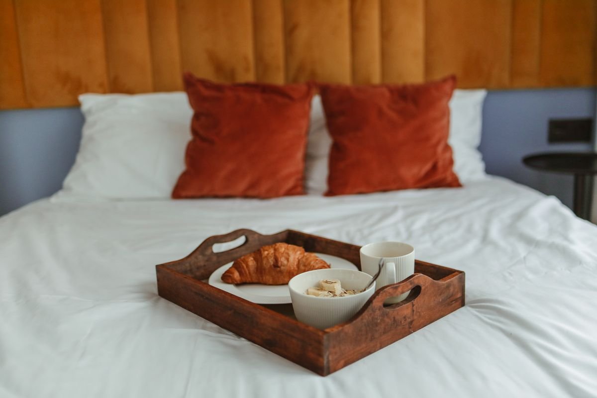 A breakfast tray with a croissant and coffee on a bed in a guesthouse room
