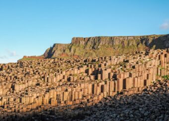 Golden light on the basalt columns of the Giant's Causeway with the cliffs behind.