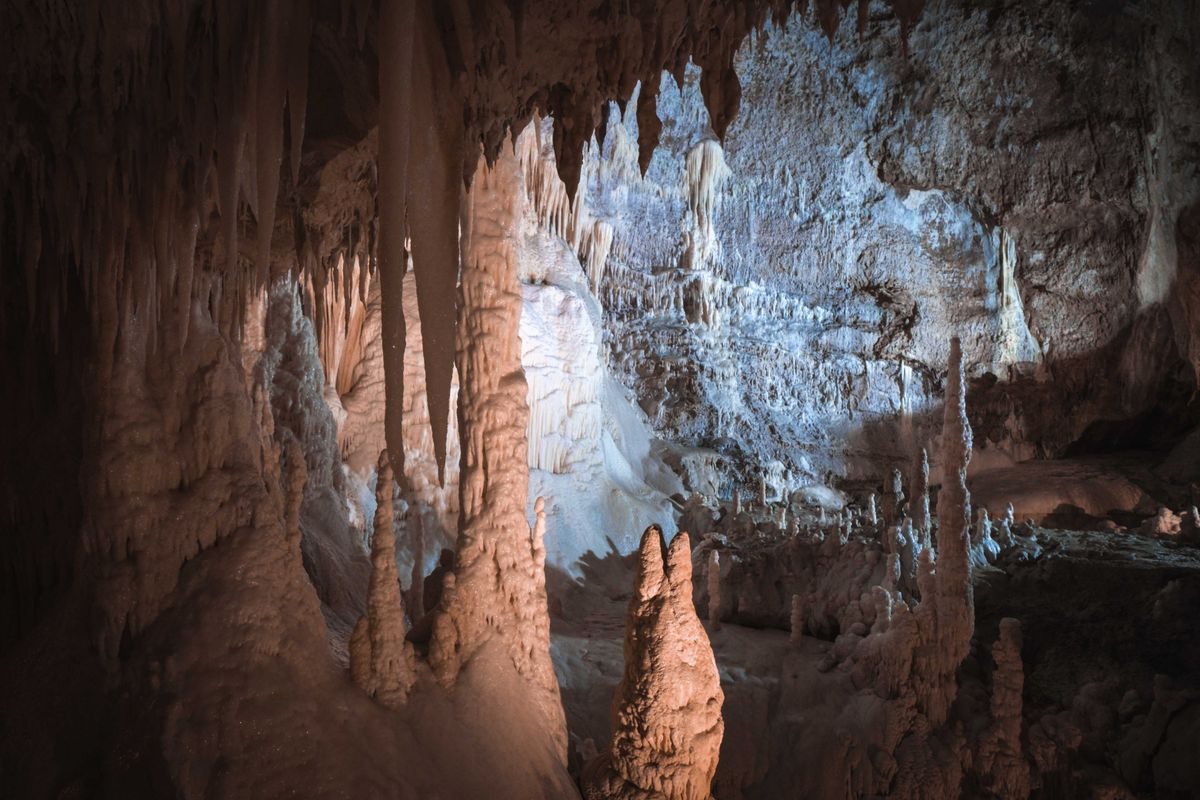 Underground cave chamber lit blue and amber with a large stalactite