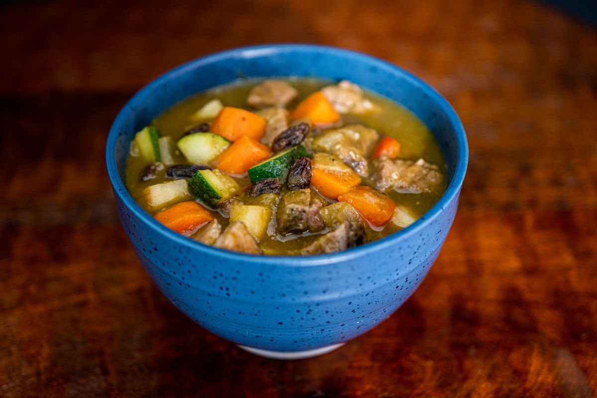 A bowl of hearty Irish stew with beef, carrots and potato on a wooden pub table