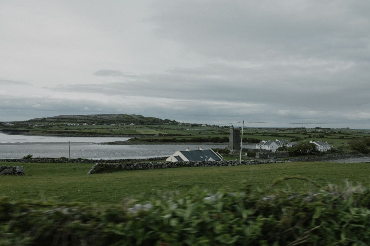 Green Irish countryside with stone walls and a coastal inlet seen from the road into Dingle