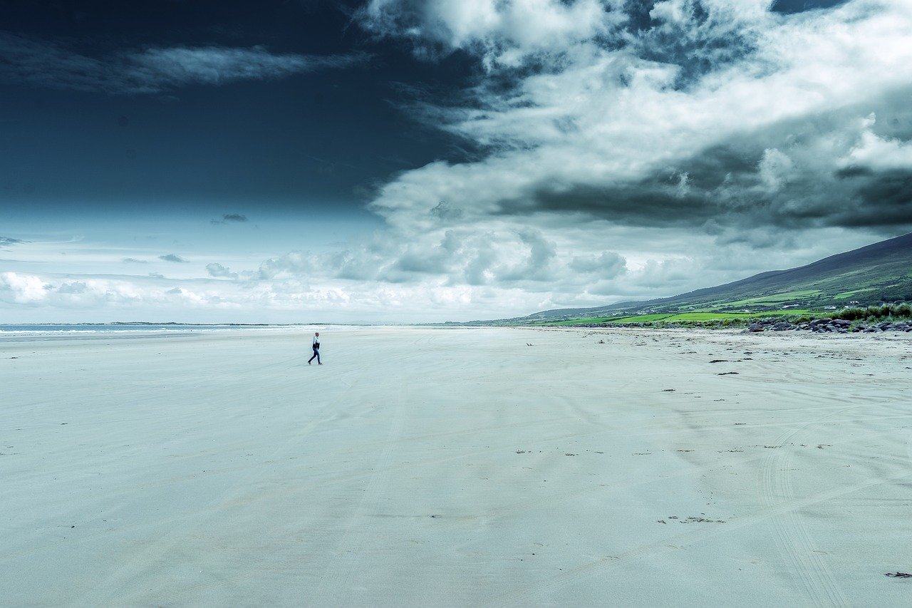 A wide empty strand and green hills under a big Irish sky