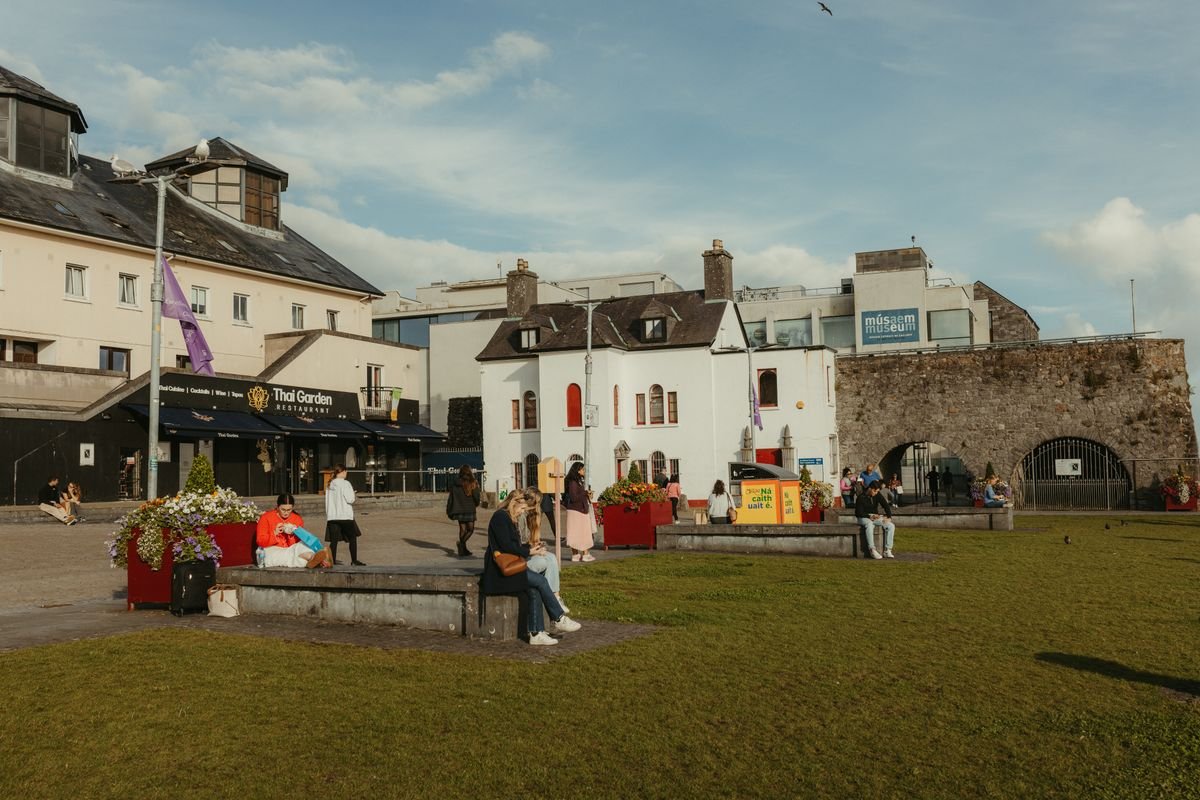 The Spanish Arch stone wall and Galway City Museum with people on the grass
