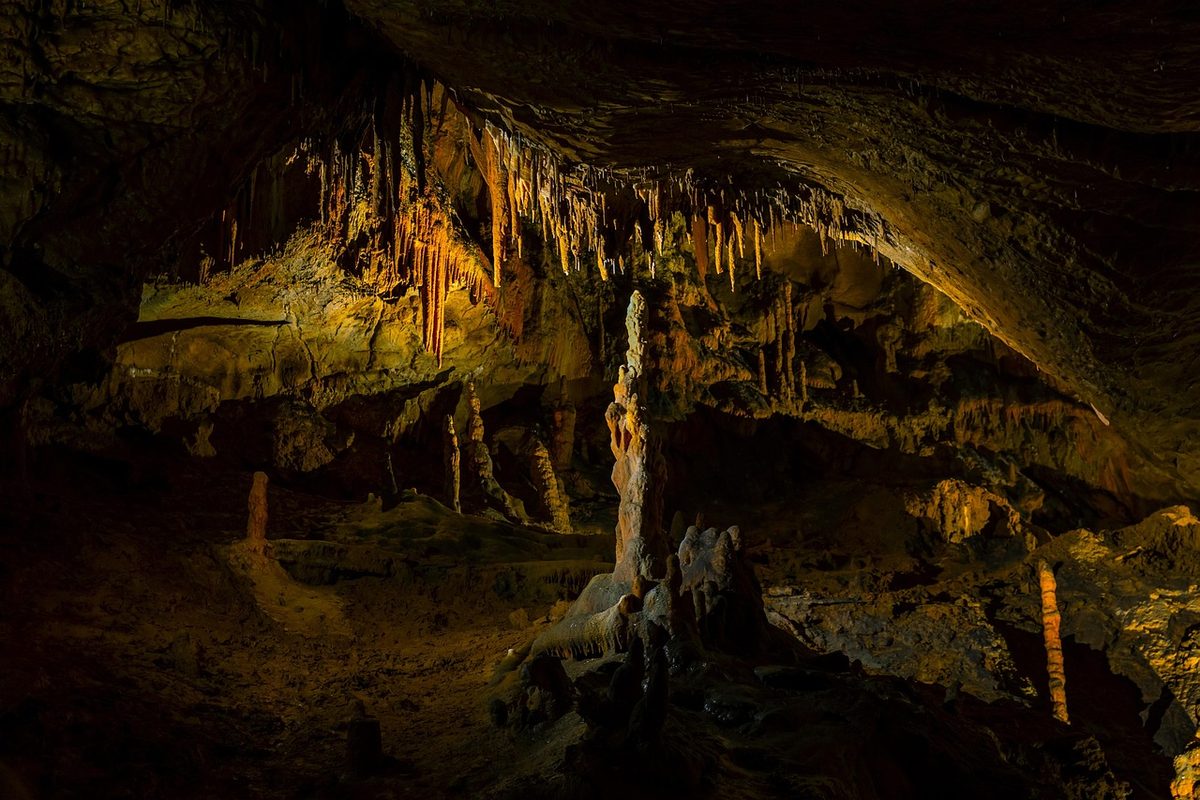 Warm-lit limestone cave with stalactites and stalagmites