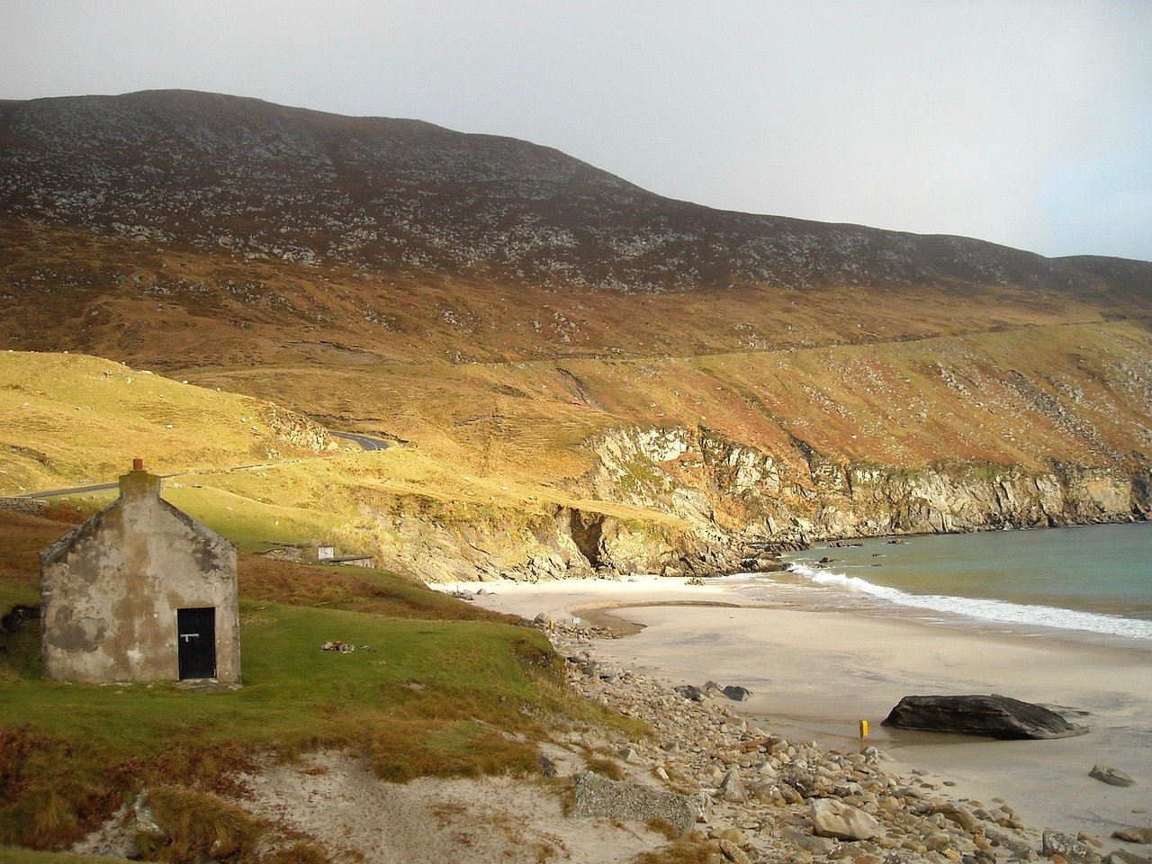 A quiet Achill Island beach with an old stone cottage below the mountain
