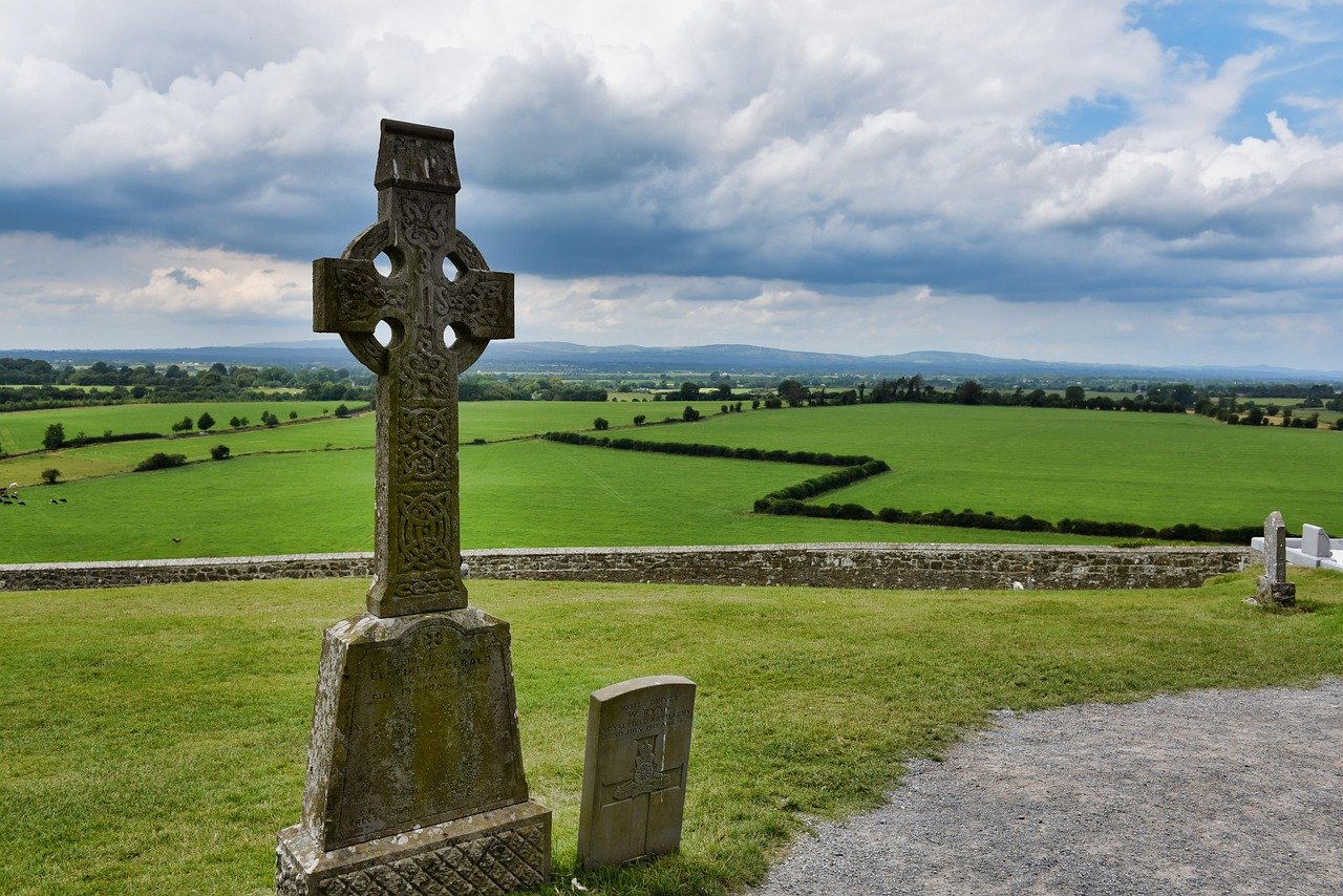A weathered high cross at the Rock of Cashel looking out over the green Tipperary plain