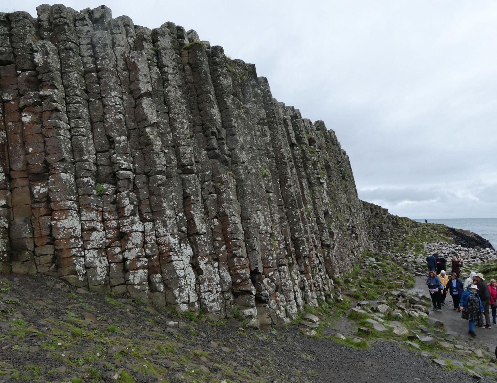 A small group on the path beside the basalt columns under a gray autumn sky