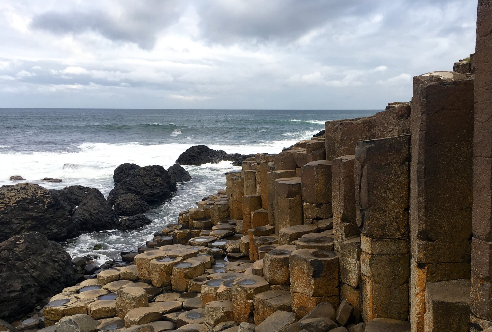 The Giant's Causeway stones empty under a gray winter sky with waves breaking behind