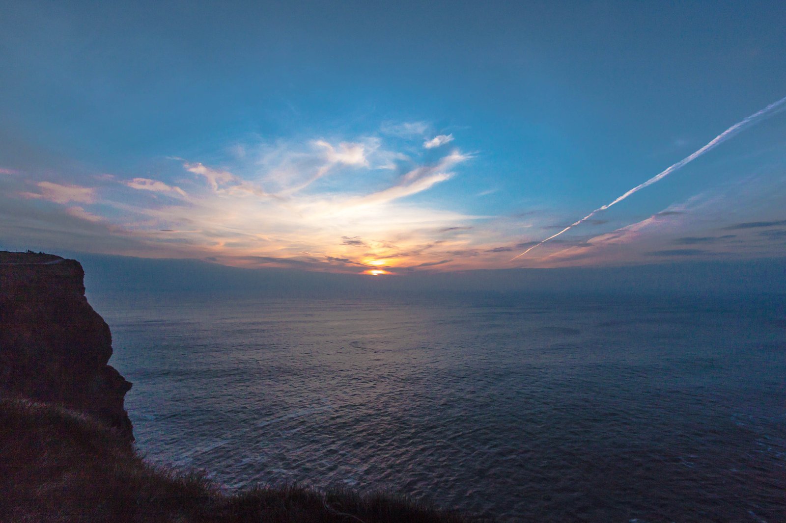 The sun setting over the Atlantic Ocean at the Cliffs of Moher with the clifftop path visible