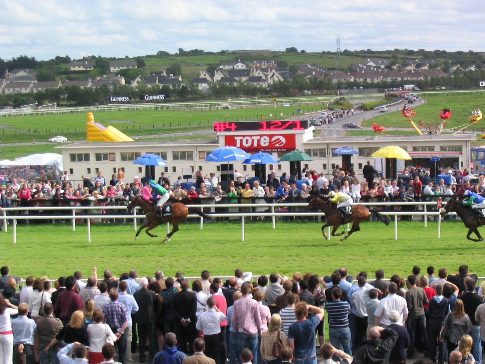 Horses racing down the track at the Galway Races with crowds watching