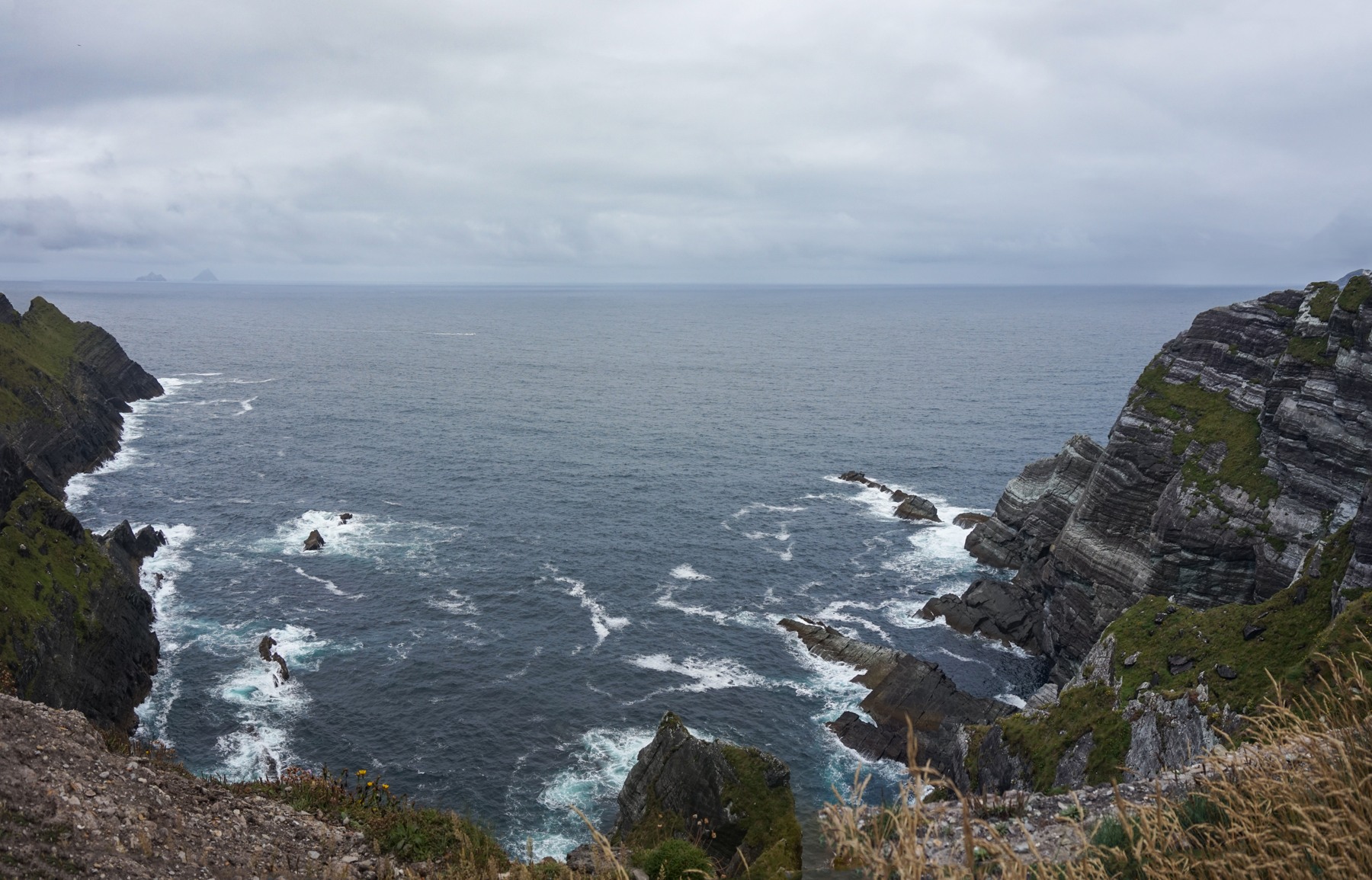 Atlantic waves between the layered rock faces of the Kerry Cliffs under gray cloud