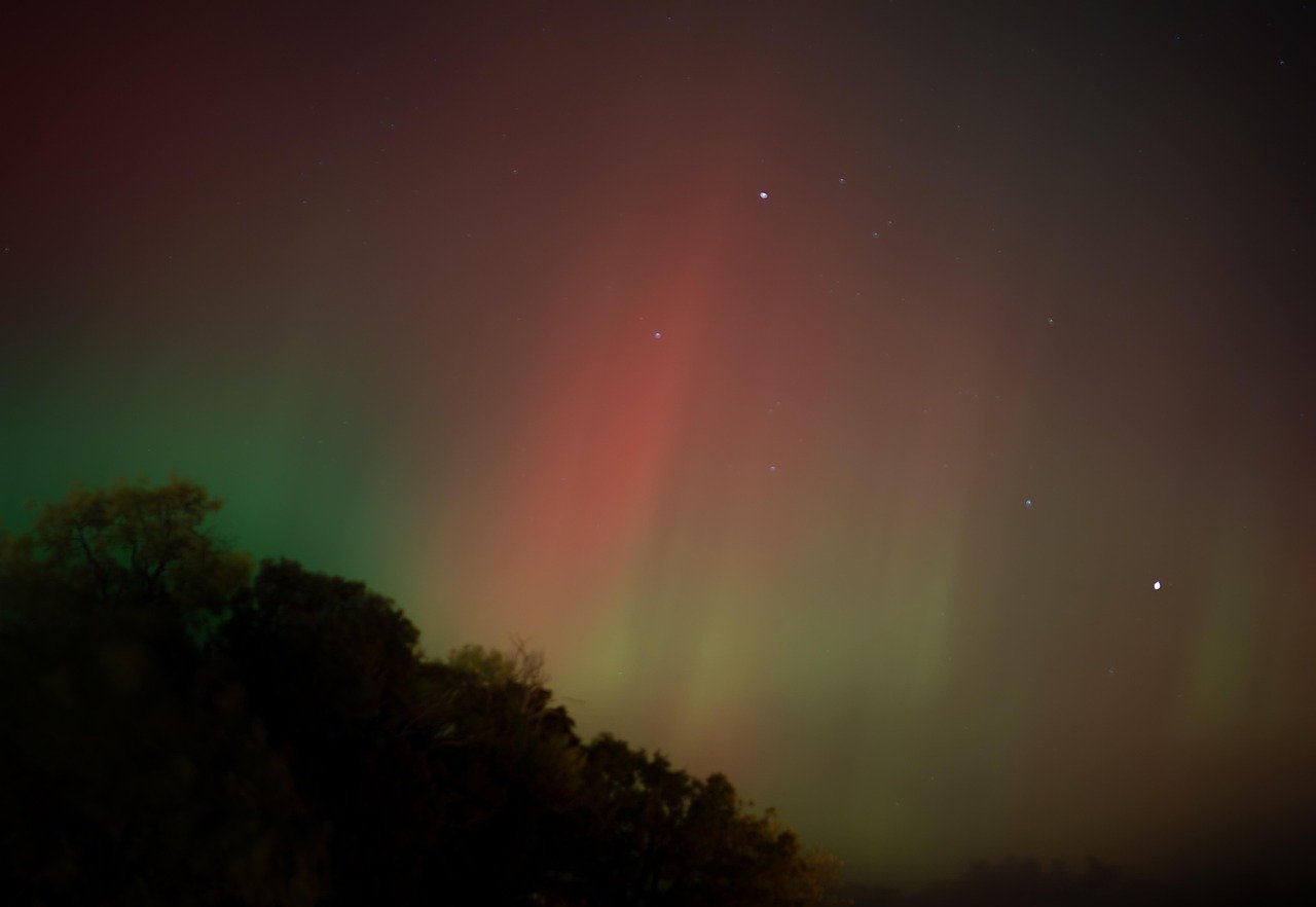 Best time to see the northern lights in Ireland: a faint red and green aurora glow over a dark treeline